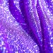An extreme close-up photograph of shimmering purple sequins and glittering fabric, capturing the glamorous and high-energy atmosphere of a major music festival performance.