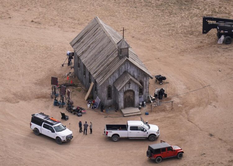 An aerial shot of an old, wooden church building surrounded by people, equipment and trucks