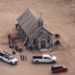 An aerial shot of an old, wooden church building surrounded by people, equipment and trucks