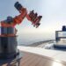 Robotic thrill ride on cruise ship deck with ocean view and outdoor screen.