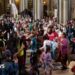 A large group of people dancing inside a church hall to a band. There is bunting across some of the internal archways in the church and there are lots of children among the dancers