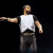Drake performing on stage, wearing a white vest and black shirt, holding a microphone. He is getting ready to release 'Iceman' his latest album.