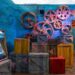 Colorful gears and crates with a circus theme against a blue wooden wall.
