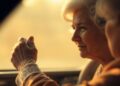 An extremely abstracted, out-of-focus photograph of an elderly woman's hands on a steering wheel, surrounded by a warm, hazy glow of light, conceptually representing the fading influence of the royal world and the universal nature of everyday challenges.