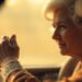 An extremely abstracted, out-of-focus photograph of an elderly woman's hands on a steering wheel, surrounded by a warm, hazy glow of light, conceptually representing the fading influence of the royal world and the universal nature of everyday challenges.