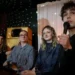 four people sit on sits in a room lit by a disco ball. the young man speaks into a microphone