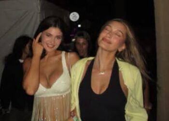 Two women in casual outfits walking together at a social event.
