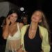 Two women in casual outfits walking together at a social event.
