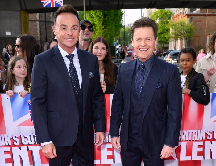 Ant & Dec stood next to each other wearing suits, smiling ahead on a red carpet.