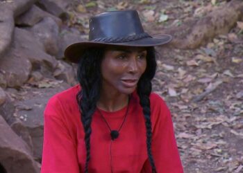 sinitta in red with black hat in jungle 2026