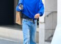 Person walking outdoors carrying a shopping bag and a phone.
