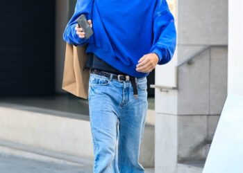 Person walking outdoors carrying a shopping bag and a phone.