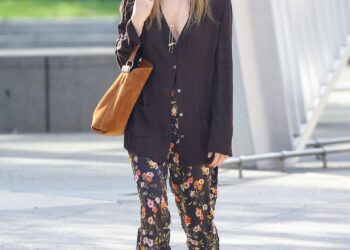Person wearing floral pants and a black cardigan walking down the street.