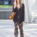 Person wearing floral pants and a black cardigan walking down the street.