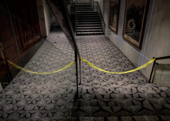 Yellow police tape blocks off a carpeted hallway with two stairways.