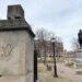Outdoors photo on a cloudy day shows a park in wintertime. Trees are bare and there's a bronze statue of George Washington riding a horse on top of a marble pedestal. In the foreground is a concrete column that shows "WS" chiseled in it.