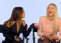 Two women seated and laughing; one in a stylish black off-the-shoulder outfit, the other in a chic pink blouse with a bow