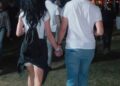 Couple walking hand in hand at an outdoor event during the evening.
