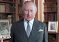 King Charles in a suit and tie with bookcases in the background