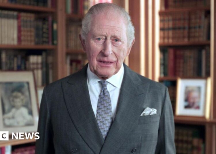 King Charles in a suit and tie with bookcases in the background