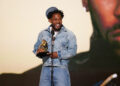 Kendrick Lamar in denim holds a Grammy award, smiling on stage. He could win the best album of the year grammy for gnx.