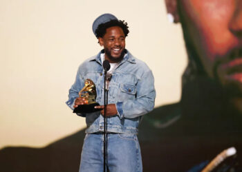 Kendrick Lamar in denim holds a Grammy award, smiling on stage. He could win the best album of the year grammy for gnx.