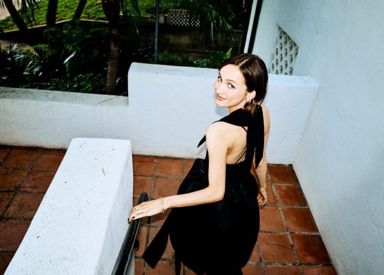 Maude Apatow descending a staircase in a black dress.