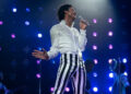 Jaafar Jackson singing on stage as Michael Jackson in a white top and striped pants in Michael movie .