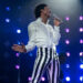 Jaafar Jackson singing on stage as Michael Jackson in a white top and striped pants in Michael movie .