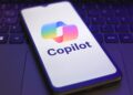 Microsoft Copilot logo and branding pictured on a smartphone screen, with smartphone placed on top of a laptop keyboard.