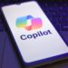 Microsoft Copilot logo and branding pictured on a smartphone screen, with smartphone placed on top of a laptop keyboard.
