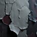 An extreme close-up of a cracked, peeling wallpaper texture in shades of gray, black, and muted red, creating a visually striking and eerie conceptual representation of the haunting atmosphere in Mitski's latest music video.