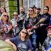 A group of 12 musicians stand with musical instruments including guitars and a tambourine on a street in Walsall, smiling at the camera.