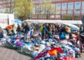 Piles of brightly colored clothes are heaped on the ground as people look through them.
