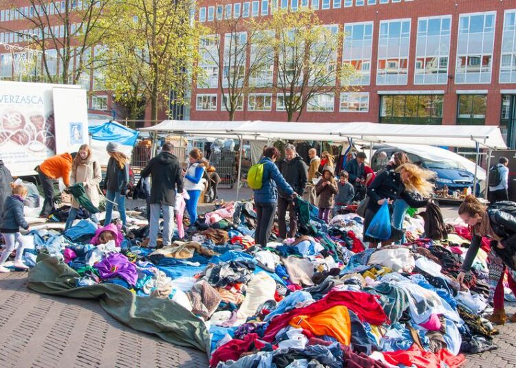 Piles of brightly colored clothes are heaped on the ground as people look through them.