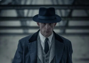 A Man in a 1950s suit walking with a serious expression on his face.