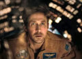 A man in a spacecraft wearing a detailed flight suit looks intensely at a screen, suggesting a scene from a space-themed film or TV show
