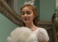 Phoebe Dynevor as Daphne Bridgerton holding a fan up. .
