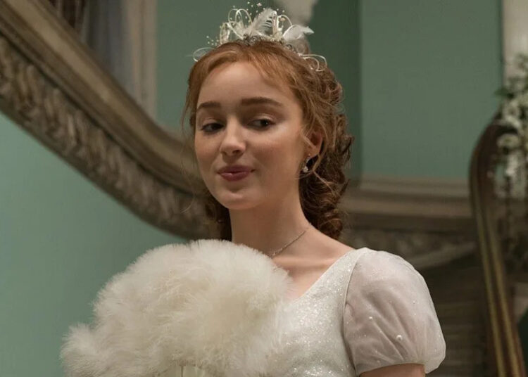 Phoebe Dynevor as Daphne Bridgerton holding a fan up. .