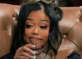 A woman with styled hair sips wine with a sly expression. Text above mentions Playboi Carti.