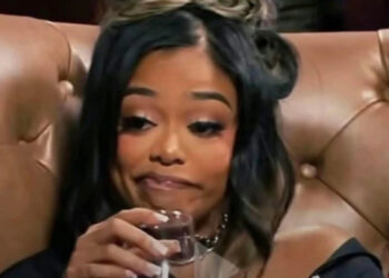 A woman with styled hair sips wine with a sly expression. Text above mentions Playboi Carti.