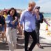 Harry and Meghan walk along Bondi Beach with surf life savers behind them.