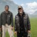 two men standing in a field with mountainous background