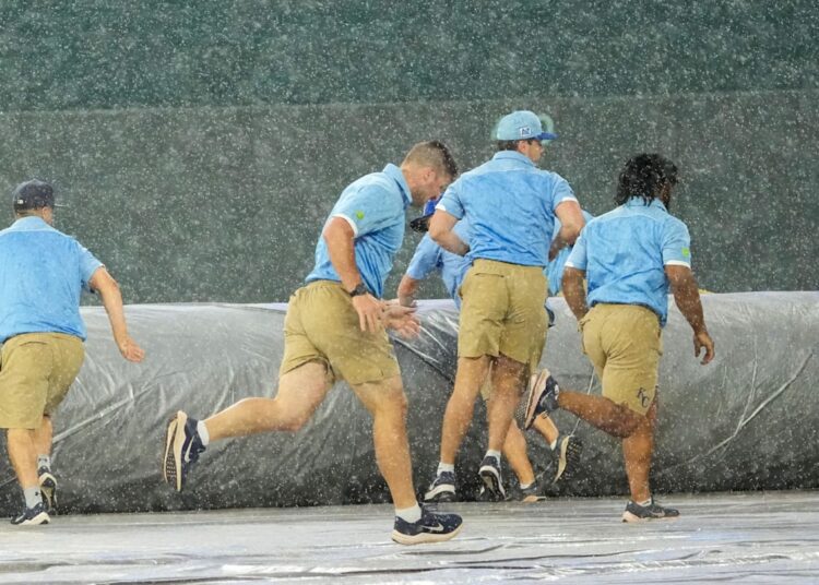 Jun 12, 2025; Kansas City, Missouri, USA; The Kansas City Royals grounds crew scrambles to spread the tarp over the field during the sixth inning rain delay of the game against the New York Yankees at Kauffman Stadium. Mandatory Credit: Denny Medley-Imagn Images