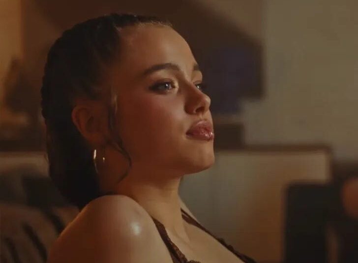 Person sitting indoors with braided hair and earrings.