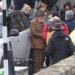 Sir Anthony Hopkins is stood by a Range Rover wearing a brown suit jacket and trousers, and a hat. He is surrounded by people from a production company for his new film.