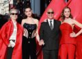 Meryl Streep, Anne Hathaway, Stanley Tucci and Emily Blunt pose on the red carpet in London. Streep is wearing sunglasses, a long, red, satin jacket, a cream blouse and black trousers. Hathaway has her hair up and is wearing a black embellished corset. Tucci is wearing a pinstriped black suit, white shirt and tie, along with sunglasses. Blunt has a red two-piece on an a jewelled necklace.
