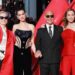 Meryl Streep, Anne Hathaway, Stanley Tucci and Emily Blunt pose on the red carpet in London. Streep is wearing sunglasses, a long, red, satin jacket, a cream blouse and black trousers. Hathaway has her hair up and is wearing a black embellished corset. Tucci is wearing a pinstriped black suit, white shirt and tie, along with sunglasses. Blunt has a red two-piece on an a jewelled necklace.