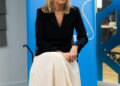 The Duchess of Edinburgh, in a black jacket and white skirt, sits in front of a Plan International banner