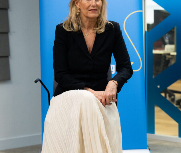 The Duchess of Edinburgh, in a black jacket and white skirt, sits in front of a Plan International banner